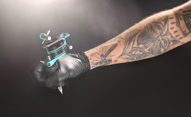 Wall Mural - Tattooist hand in medical glove with tattoo machine on black background