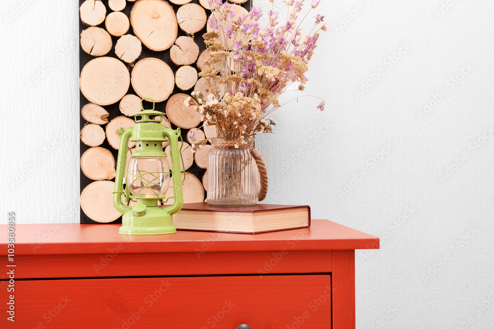 Room interior with red wooden commode, flowers and lantern on light wall background