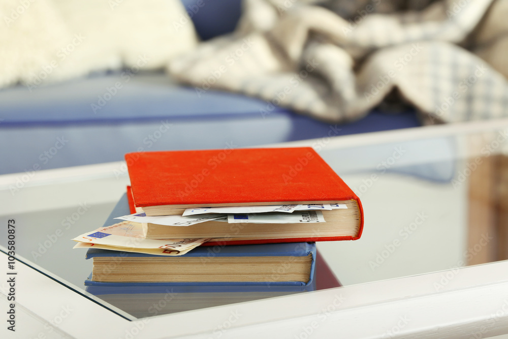 Red and blue books with hidden euro banknotes on glass table