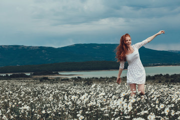 Wall Mural - Beautiful young girl with curly red hair in chamomile field