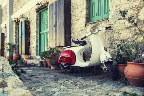 Fotomural Old scooter parked by the wall in the empty street of Karpathos, Greece