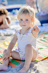 a little girl sits on the beach in the sand and smiles