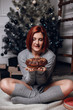 © Olena_Molchanova - fashion interior photo of beautiful young woman with red hair and charming smile, wears cozy knitted cardigan, posing beside Christmas tree and presents with chocolate cake with asterisks