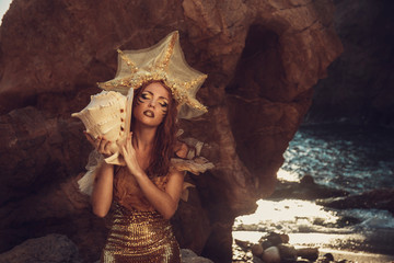 Beautiful fashionable mermaid sitting on a rock by the sea