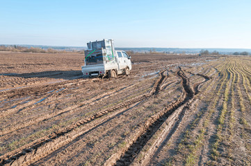 Wall Mural - Off-road truck with furniture settles down in mud on dirty road in fallow field
