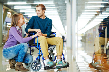 Amorous girl looking at her boyfriend in wheelchair in the mall