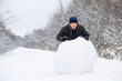 © fotoduets - Boy rolls a big snowball to build a snowman in winter day