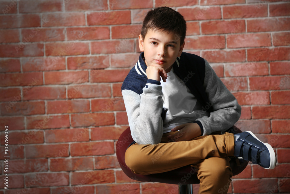Cute little boy sitting on a chair near brick wall
