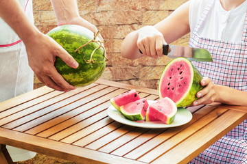 Canvas Print - Young woman in apron slicing fresh ripe juicy red watermelon