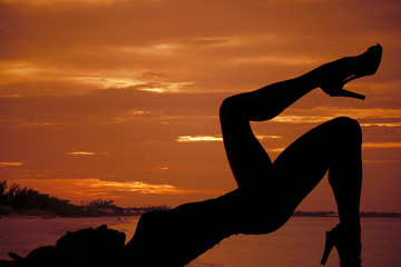 Wall Mural - silhouette of woman by water in sunset lay on back leg up