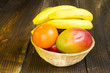mango,klementynki i banany w wikinowym koszyczku na drewnianym tle