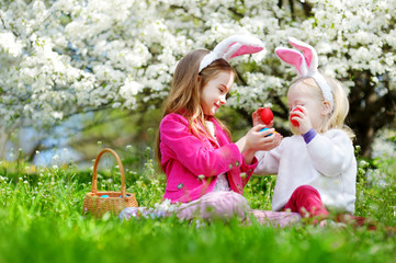 Wall Mural - Two adorable little sisters hunting for easter egg in blooming spring garden