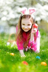 Wall Mural - Adorable little girl hunting for easter egg in blooming spring garden