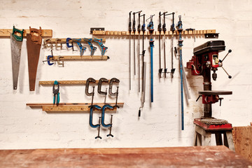 Workshop wall with tools in rows alongside a drill press