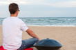 Young stylish guy sitting on the sand beach near handpan or hang with sea On Background. The Hang is traditional ethnic drum musical instrument