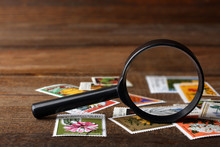 A Small Pile Of Expensive And Collectible Stamps With A Magnifying Glass On Wooden Brown Table
