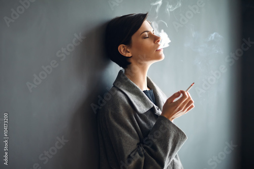 Fotografía Portrait of fashionable woman smoking a cigarette on dark backgr