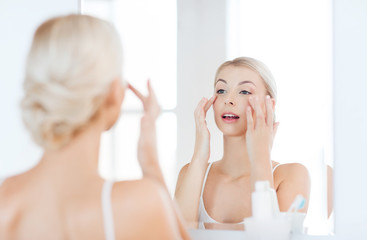 happy woman applying cream to face at bathroom