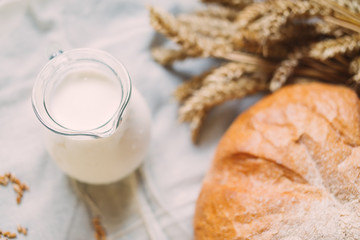 Glass jug with milk and bread on white textile