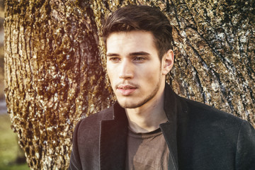 Wall Mural - Handsome young man leaning against tree