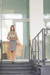 © bokan - Smiling young businesswoman portrayed at the top of the stairs in front of her office