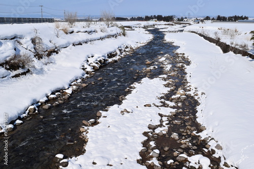 小川の雪溶け 冬は長い期間 鉛色の雲に被われる雪国の山形県ですが 春が近くなり 久し振りの好天で雪が溶け始めました 小川の雪溶け水がせせらぐ風景を撮影した 春の息吹を感じる早春イメージの写真です Stock Photo Adobe Stock