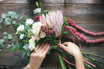 Florist at work: pretty young blond woman making fashion modern bouquet of different flowers