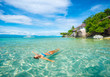Woman in bikini relaxing lying on water against background of beach and bungalow.