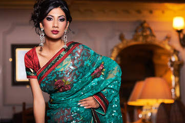 Unique portrait of oriental indian indoor model dressed with colorful saree and wearing asian jewellery and strong makeup