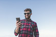© Westend61 - Spain, La Coruna, portrait of smiling hipster with sunglasses looking at his phablet in front of blue sky
