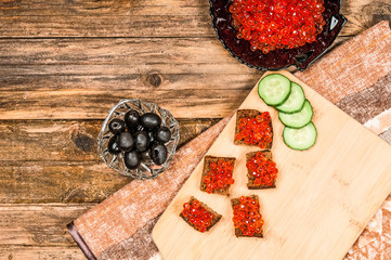 Toasts with red caviar with olives and cucumbers on wooden backg