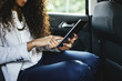 © Westend61 - Young woman sitting on back seat of a car using mini tablet, close-up