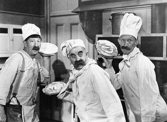 Three chefs holding pies for a fight in the kitchen 