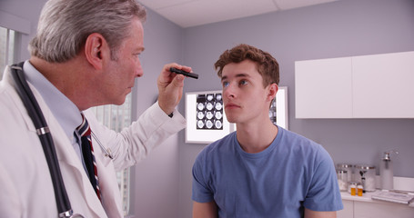 Mid-aged doctor examining eyes of young adult male patient