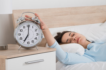 Woman Turning Off Alarm While Sleeping On Bed