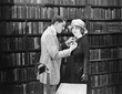 Profile of a young man attaching a brooch on a young woman's overcoat in a library 