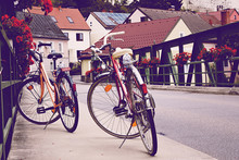 Two Old Bicycle On The Bridge In Vintage Tinting. Romantic Urban Landscape In A Small European Town In Austria.