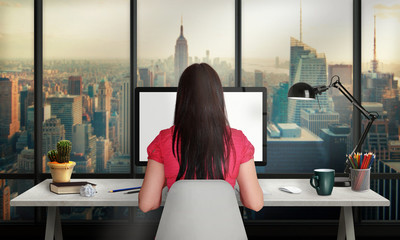 Aufkleber - Woman work on office computer with isolated screen for mockup. Office with a view of the skyscrapers. Desk with lamp, plant, coffee, pencils, book.