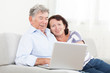 © kraevski - Senior couple laughing while using laptop