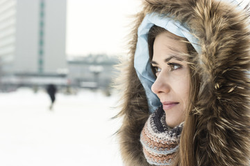 cute girl wearing blue coat with fur hood on and a scarf walking down the winter city streets