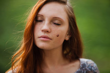 Beautiful Redhead Girl With Freckles On A Background Of Green Grass With Ladybird On The Cheek 