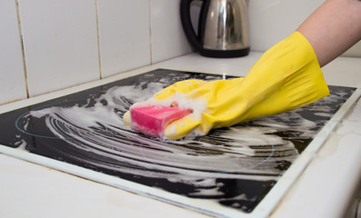 Cleaning hand in a yellow rubber glove washes a plate in the kitchen