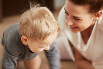 Young mother with her one years old little son dressed in pajamas are relaxing and playing in the bedroom at the weekend together, lazy morning, warm and cozy scene. Pastel colors, selective focus.