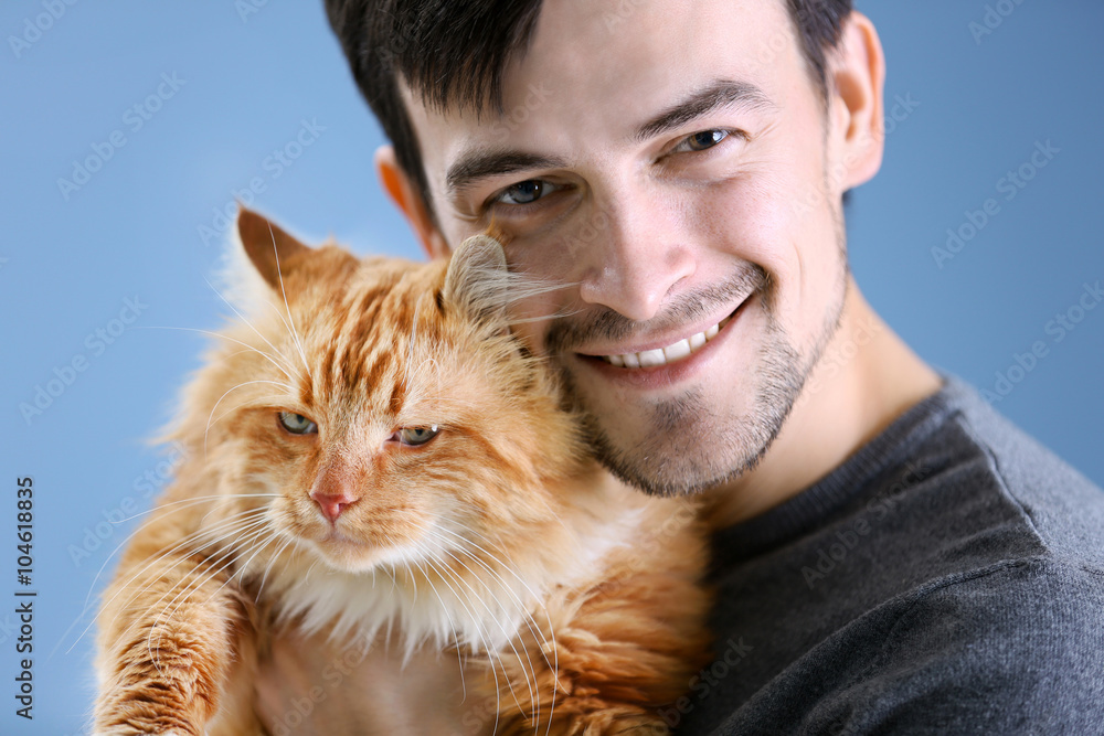 Smiling young man holding a fluffy red cat