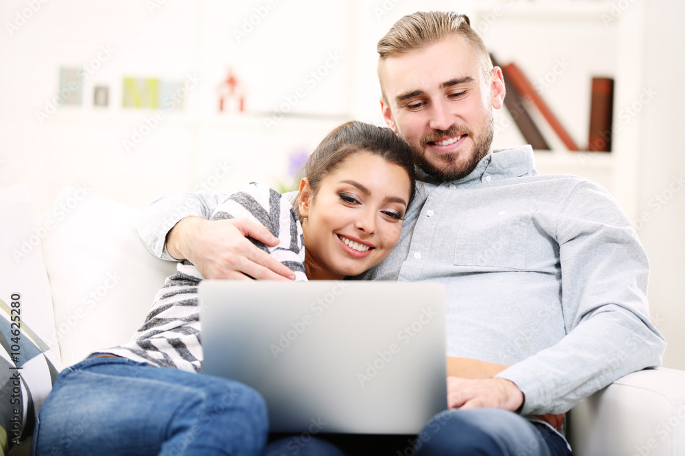 Happy couple sitting on sofa and working on a laptop