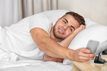 Wall Mural - Beautiful young man waking up with mobile alarm clock