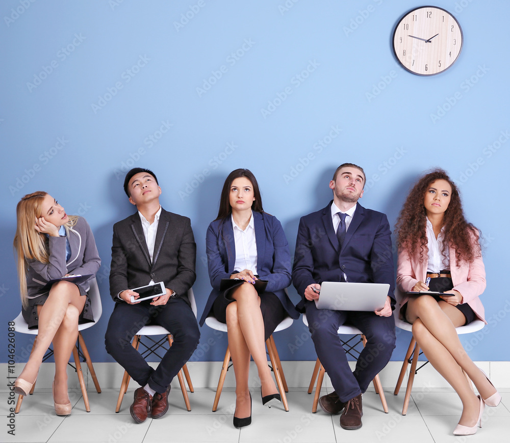Young people sitting on a chairs and looking at the clock in blue hall