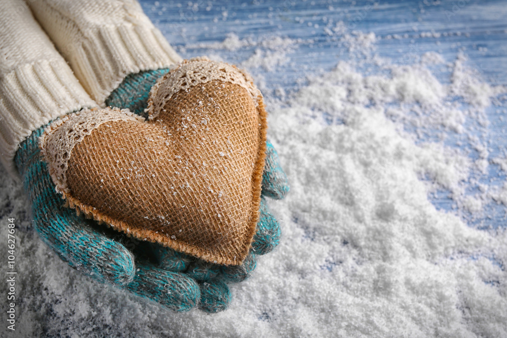 Female hands in mittens with decorative heart on snow background