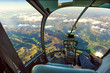 Helicopter cockpit flying on mountain landscape and cloudy sky, with pilot arm driving in cabin. Spectacular aerial view of Alps mountain chain.
