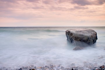romantic atmosphere in peaceful morning at sea. big boulders sticking out from smooth wavy sea. pink